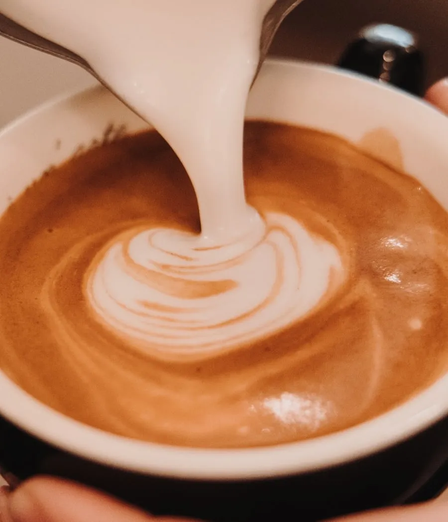 Milchschaum wird in eine Tasse Espresso gegossen und formt ein Latte-Art-Muster