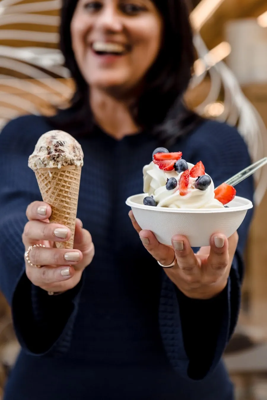 Lachende Gastgeberin hält einen Becher Frozen Yoghurt mit Beeren und eine Waffeltüte